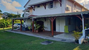 A two-story house with a covered porch, a car parked in front, and a well-maintained lawn. - RENTAL 5 ROOM SUN HOLLIDAYS ANY COMFORT SAINTE-ANNE GUADELOUPE (Sainte-Anne)