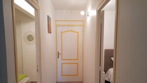 A narrow hallway with a door at the end, a bed with a green pillow, and a chair in the adjacent room. - RENTAL 5 ROOM SUN HOLLIDAYS ANY COMFORT SAINTE-ANNE GUADELOUPE (Sainte-Anne)