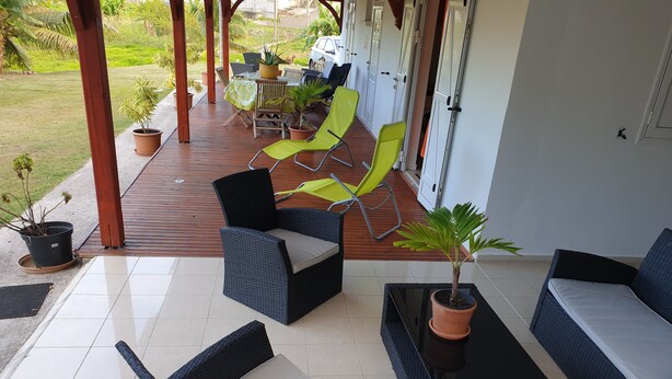 A covered outdoor seating area with wicker furniture, potted plants, and a view of the garden. - RENTAL 5 ROOM SUN HOLLIDAYS ANY COMFORT SAINTE-ANNE GUADELOUPE (Sainte-Anne)