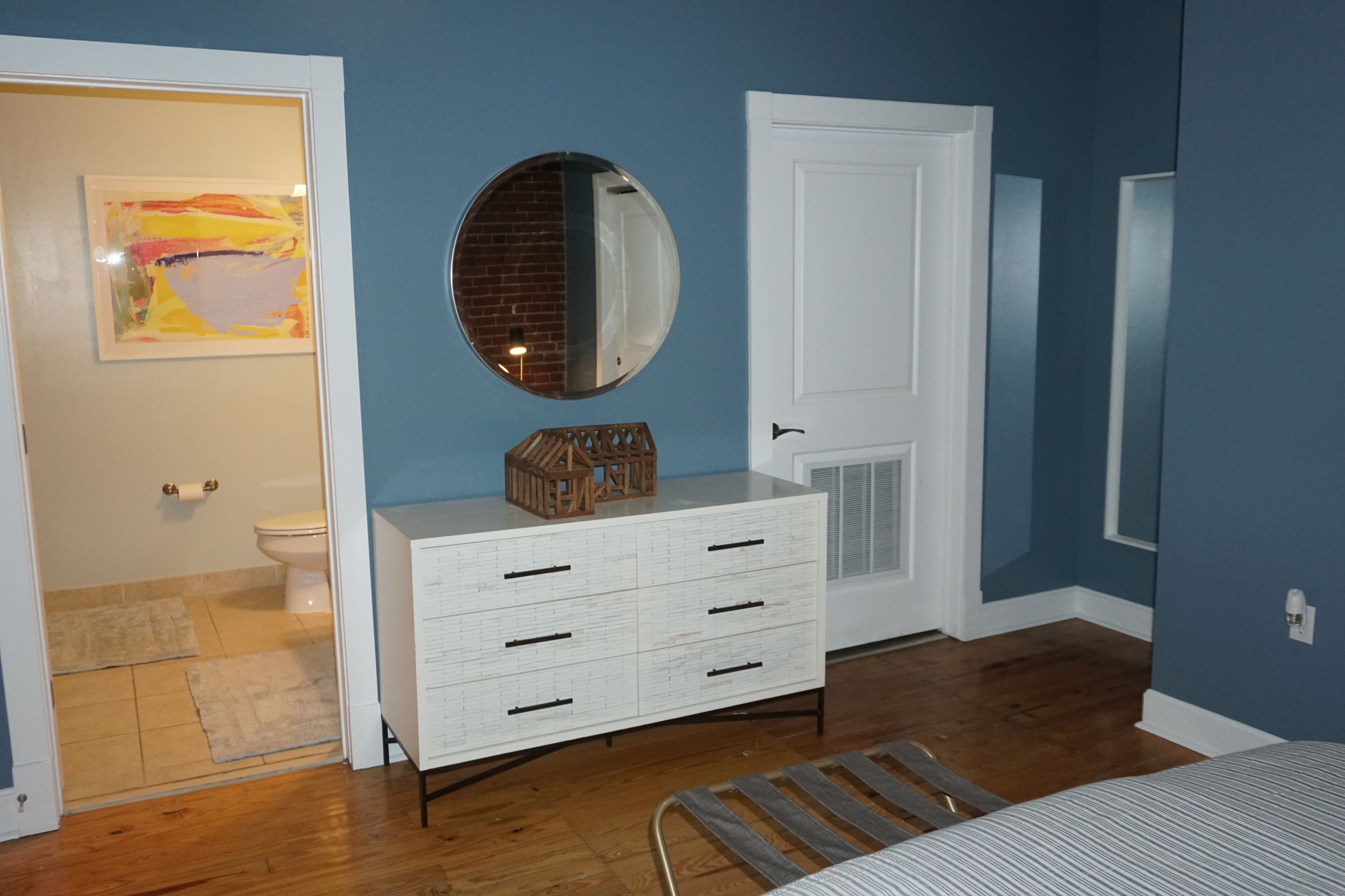 Une chambre à coucher avec un lit, une commode, un miroir et une porte.