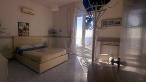 A bedroom with a bed, a bedside table, a chair, a small table, and a window with curtains. - Seaview dream home (Conca dei Marini)