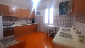 A kitchen with wooden cabinets, a refrigerator, a stove, and a sink. There is a window providing natural light and a tiled backsplash. - Seaview dream home (Conca dei Marini)