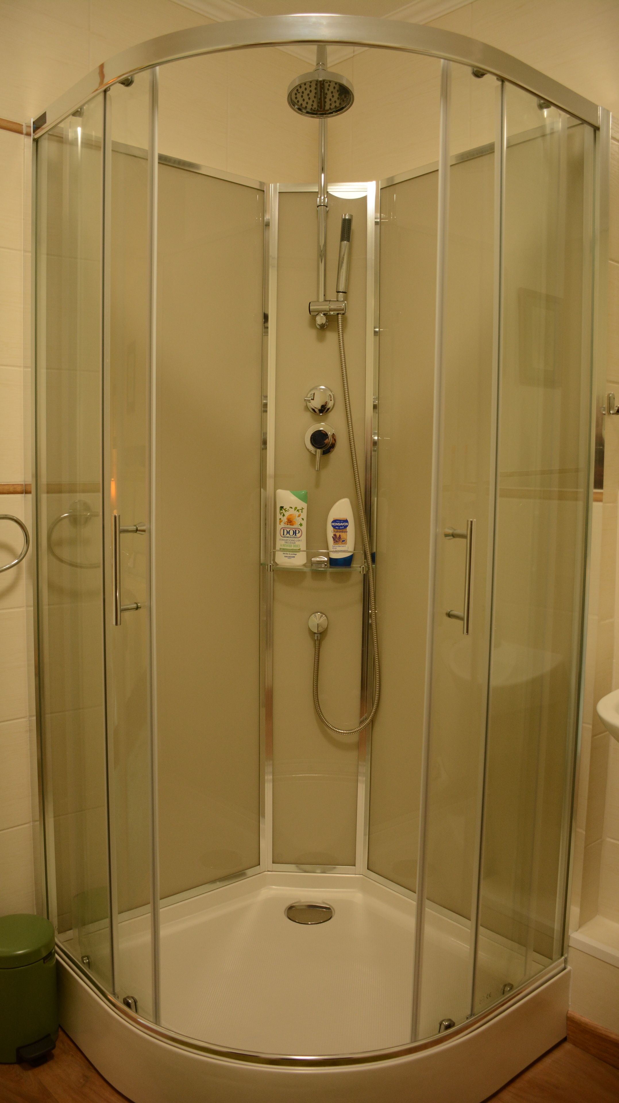 Cabina de ducha con paredes de vidrio, ducha de mano y un dispensador de champú y acondicionador.
