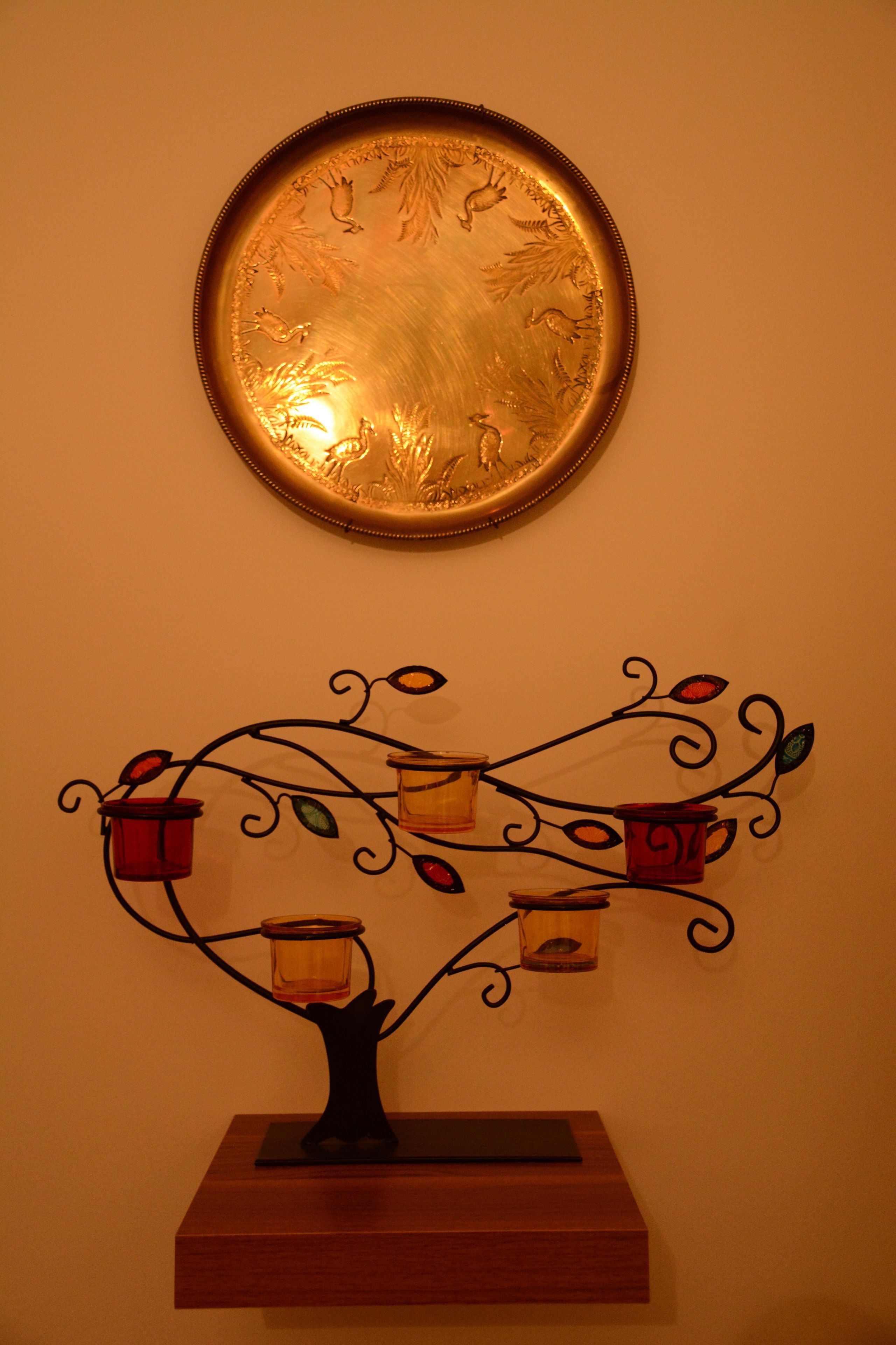 A wall-mounted decorative piece with a circular mirror and a metal tree-like structure with candle holders.