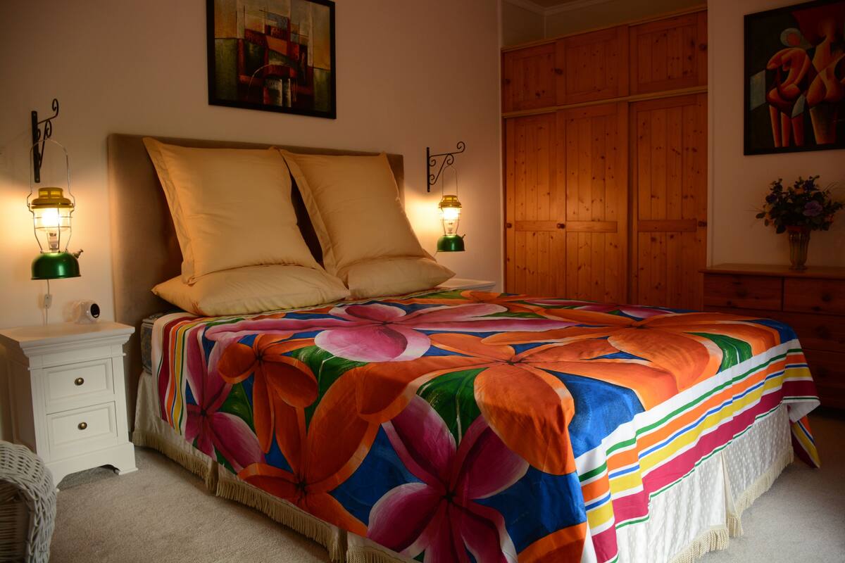 Ein Schlafzimmer mit geblümter Bettdecke, zwei Nachttischlampen, einem weißen Nachttisch und einem Holzschrank.
