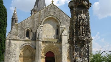 Una iglesia antigua con una aguja destacada, una entrada arqueada grande y una cruz de piedra en primer plano.