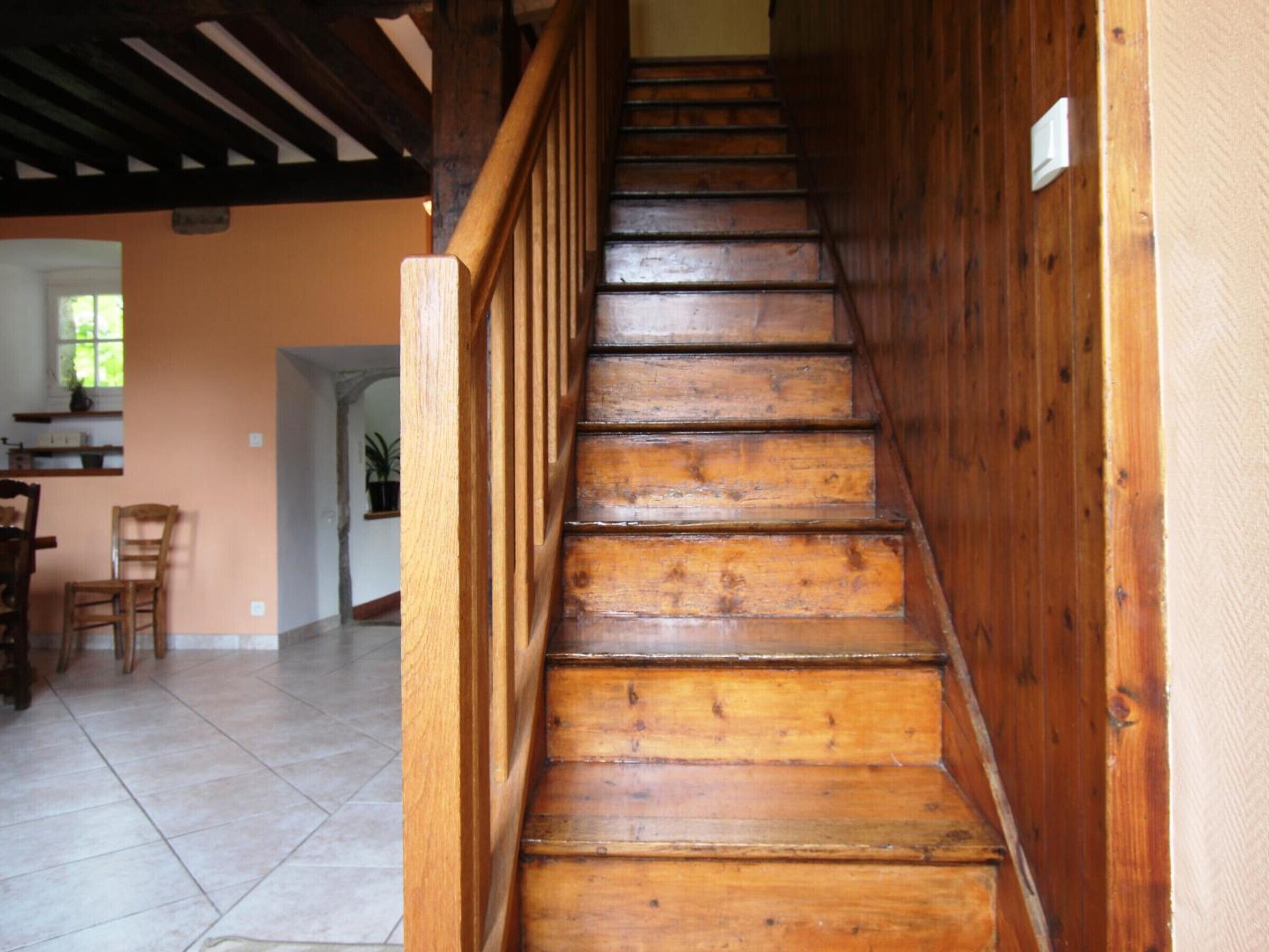 Unes escales de fusta amb barana, que condueixen a una habitació amb terra de rajola i una cadira.