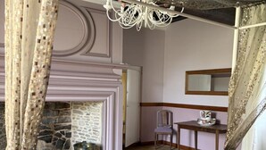 Ein Zimmer mit Kamin aus Stein, einem Holzstuhl, einem Tisch mit Tasse und einem Spiegel an der Wand.