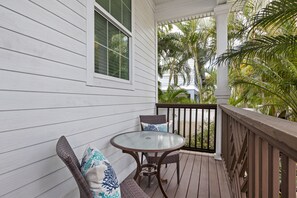 A wooden deck with a glass table and wicker chairs, surrounded by white siding and palm trees. - Minnie Cottage- Beautiful 3 bedroom heated pool/spa and short walk to the beach (Holmes Beach)