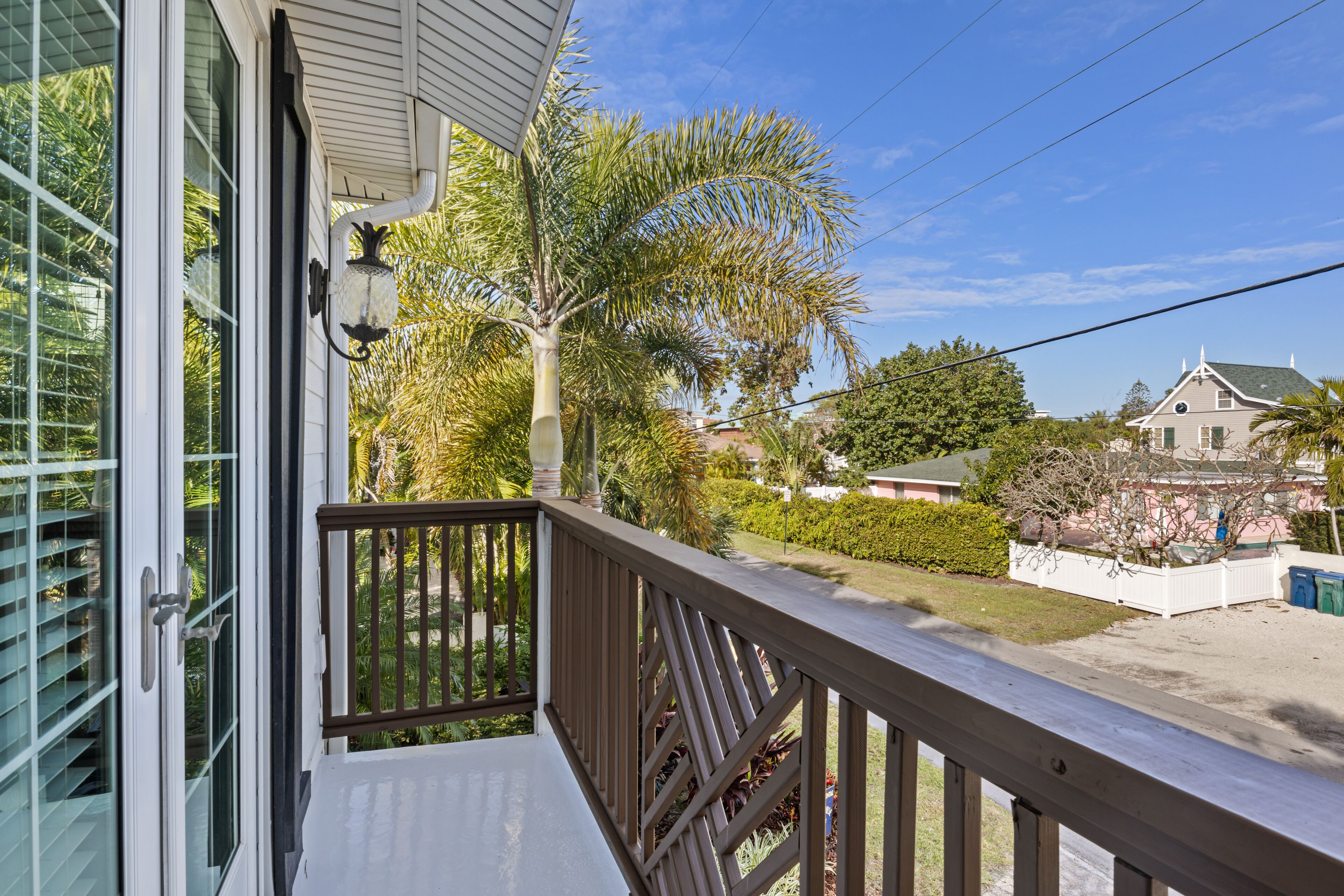 A wooden deck with a railing, a glass door, and a view of a residential area with houses and trees.