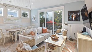 A sunlit room with a ceiling fan, a dining table with chairs, a sofa with cushions, wicker furniture, and artwork on the walls. - Minnie Cottage- Beautiful 3 bedroom heated pool/spa and short walk to the beach (Holmes Beach)
