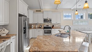 A modern kitchen with white cabinetry, stainless steel appliances, a granite countertop, and pendant lighting. - Minnie Cottage- Beautiful 3 bedroom heated pool/spa and short walk to the beach (Holmes Beach)