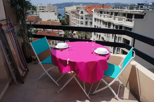 A balcony with a table set for two, chairs, and a view of the cityscape.