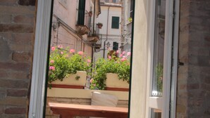 Puerta abierta que da a un balcón con una mesa de madera y plantas en macetas.