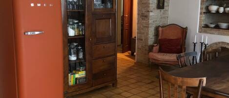 A kitchen with a tiled floor, a wooden cabinet with glass doors, a vintage orange refrigerator, and a dining table with chairs.
