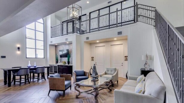 A spacious living area with a high ceiling, a staircase, and a kitchen area.