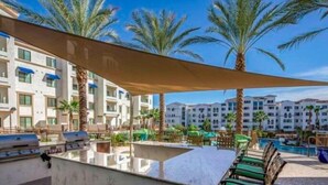 A poolside area with a grill, lounge chairs, and palm trees.