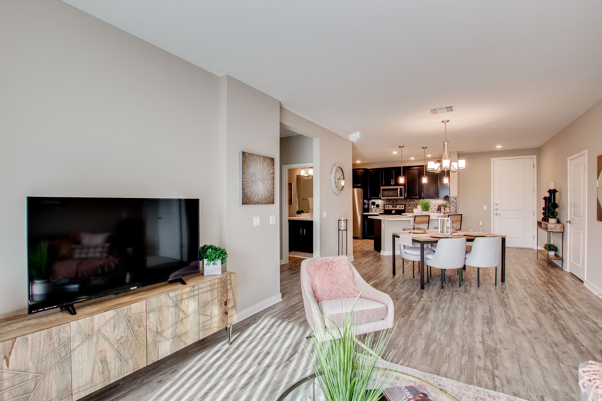 A modern living room with a flat-screen TV, a dining area with a table and chairs, and a kitchen in the background.