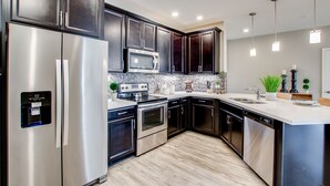 A modern kitchen with stainless steel appliances, dark wood cabinets, and a white countertop.
