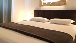 Hotellihuone, jossa on sänky, kattotuuletin, seinään kiinnitetty valaisin ja taulu.