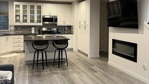 A modern kitchen with white cabinets, a central island with stools, a built-in microwave, and a fireplace. - New centrally located townhouse with rooftop deck. Walk to restaurants and shops (Seattle)
