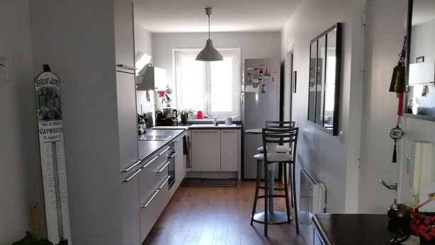 A modern kitchen with wooden flooring, a dining area with a chair, and a hanging light fixture. - Bohemian chic apartment in the heart of the Antigone district (Montpellier)