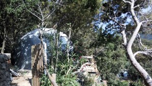 A stone pathway leading to a wooden gate, surrounded by dense foliage and a large dome structure. - Eremo di Montevergine : Seaview Dome, suspended between sky and sea (Forio)