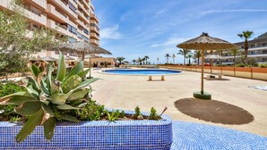 Ein Poolbereich eines Resorts mit großem Pool, Liegestühlen und einem Gebäude mit Balkonen.