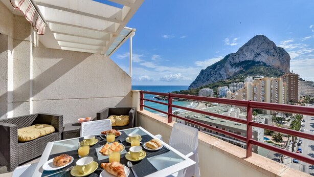 Ein Balkon mit Frühstückstisch, mit Blick auf eine Küstenstadt und einen markanten Berg.