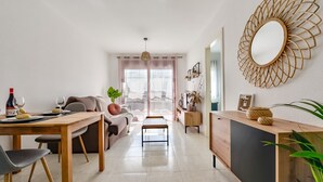 Ein modernes Wohnzimmer mit Essbereich, einer Couch, einem Couchtisch und einem Fernseher. An der Wand befindet sich ein großes Spiegelbild und eine Pflanze steht daneben.