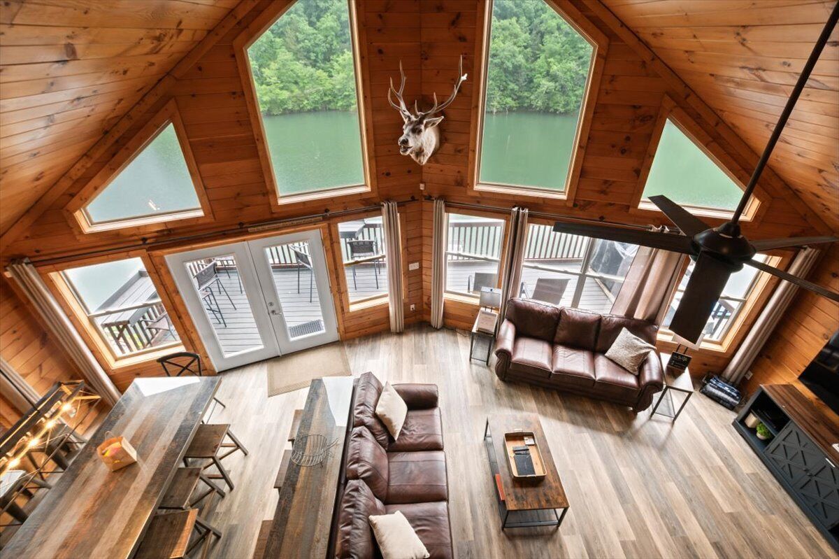 Un chalet confortable avec un intérieur en bois, une grande table à manger, un canapé en cuir et une tête de cerf fixée au plafond.