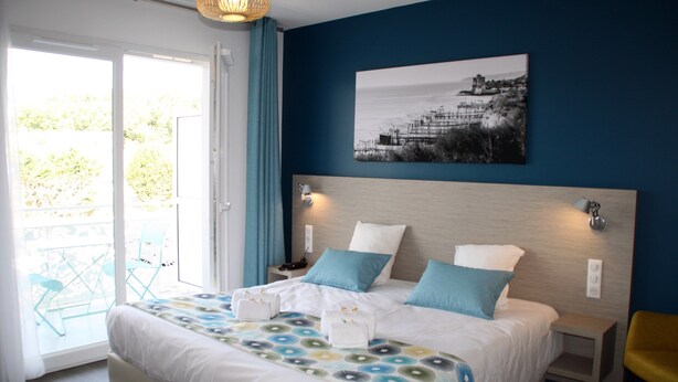 Un dormitorio con cama, mesita de noche, lámpara de pared y ventana con cortinas.