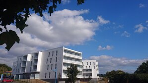 Un edificio moderno de varios pisos con balcones, un estacionamiento y un cielo despejado.