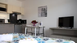 Habitación de hotel pequeña con cama, una mesita de comedor con sillas, kitchenette, televisión y un cuadro en la pared.