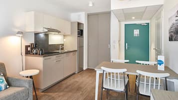 A compact kitchen with modern appliances, a dining area with a table and chairs, and a teal door.