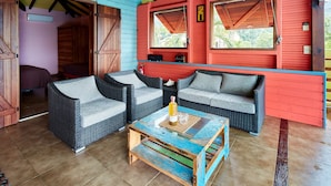 A cozy room with wicker furniture, a wooden coffee table, and a red wall. - Villa Mangotine, luxury villa in deshaies in Guadeloupe (Deshaies)