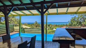 A covered outdoor area with a pool, dining table, and chairs, overlooking a scenic view of the ocean. - Villa Mangotine, luxury villa in deshaies in Guadeloupe (Deshaies)