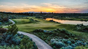 Un campo de golf con un estanque, árboles y una puesta de sol al fondo.