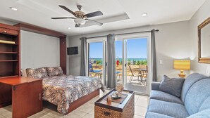 Una camera da letto con un letto, una scrivania, un divano, una ventola a soffitto e vista sulla spiaggia attraverso le porte scorrevoli.