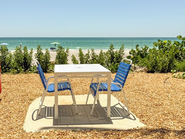 A table and two chairs on a pebble-covered surface with a view of the ocean. - THE BEACH CONDO #107 BEACHFRONT FULL VIEW (Longboat Key)
