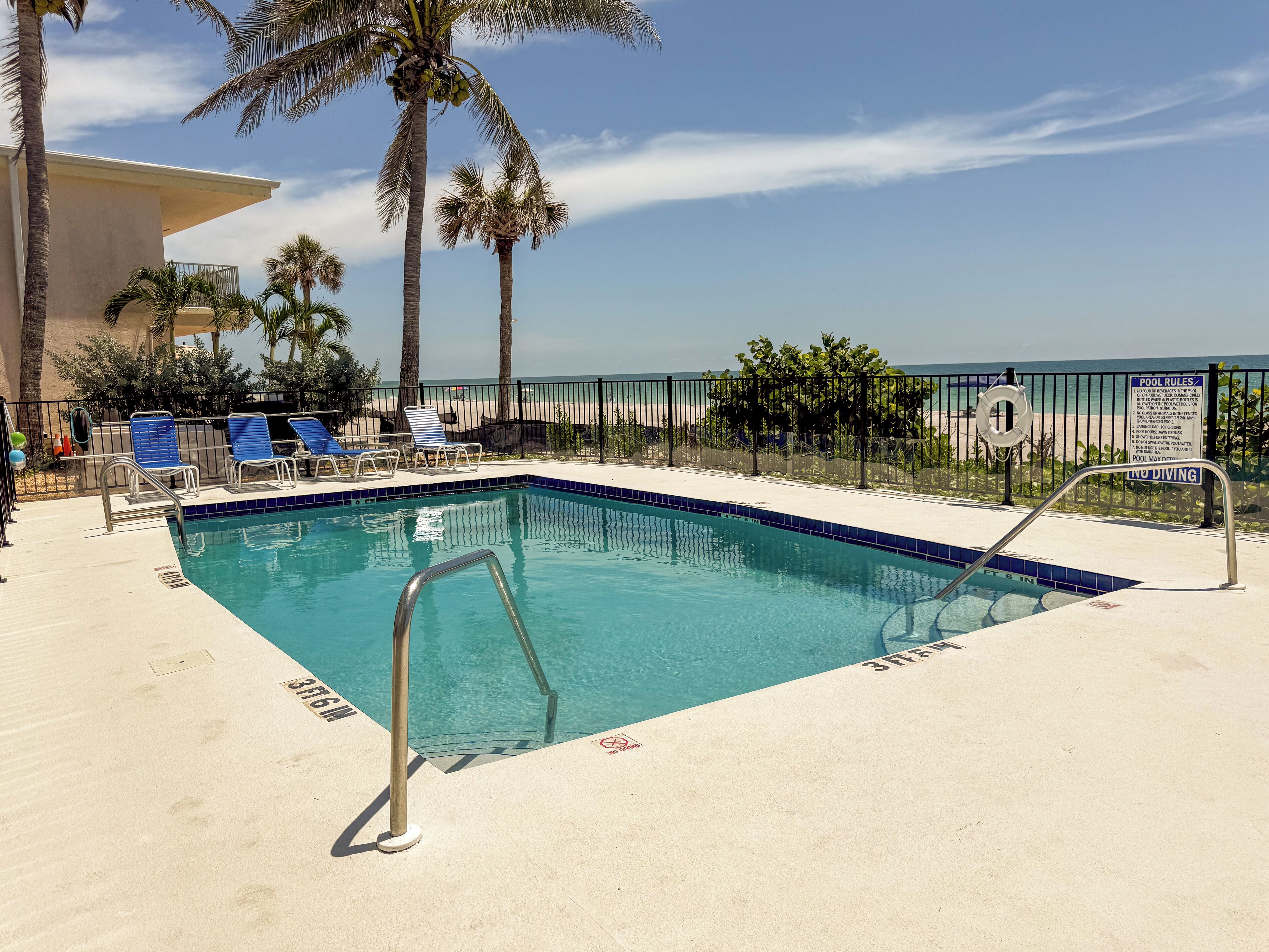Un espace piscine avec une eau d’un bleu limpide, des chaises longues, des palmiers et une vue sur la plage.