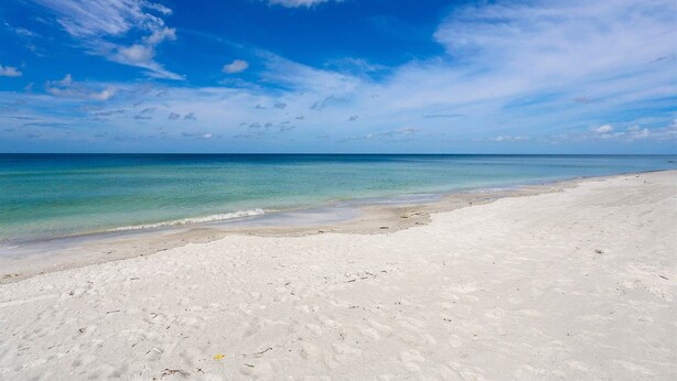 Ampia spiaggia sabbiosa con acque cristalline turchesi e cielo azzurro.