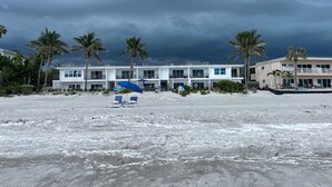 Een hotel aan het strand met meerdere balkons, een zandstrand en palmbomen.