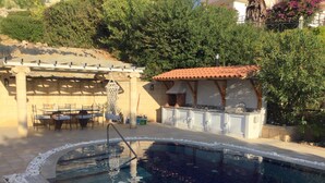 A swimming pool with a stone border, a pergola, and a covered patio area with tables and chairs. - Villa Helios with Private Pool,New outside kitchen and BBQ,  welcome pack inc... (Kalathos)