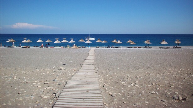 A beach with a wooden walkway leading to the sea, lined with thatched umbrellas. - Villa Helios with Private Pool,New outside kitchen and BBQ,  welcome pack inc... (Kalathos)