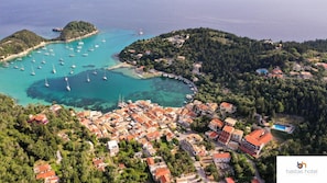 Vista aérea de uma cidade costeira com um porto de iates, casas com telhados vermelhos e um mar azul cristalino.