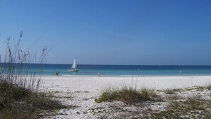 Une plage avec un voilier, un ciel bleu clair et une mer calme.