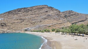 Une plage avec une eau d’un bleu limpide, un rivage sablonneux et des collines rocheuses en arrière-plan.