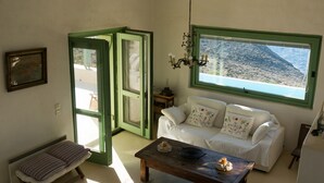 Une pièce avec un canapé blanc, un banc, une table en bois, un lustre et une fenêtre donnant sur un paysage montagneux.