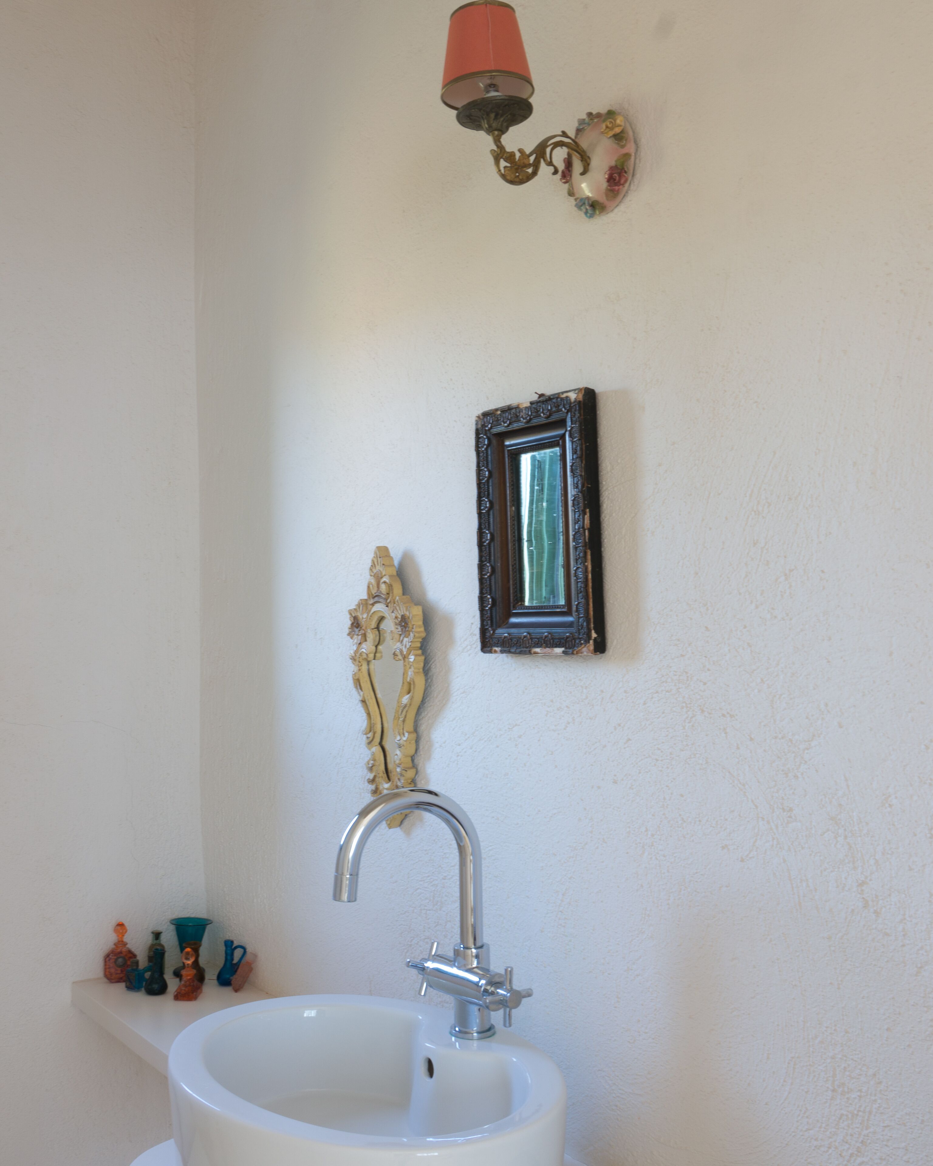 Een badkamer met een witte wastafel, een spiegel, een decoratief wandobject en een rode wandlamp.